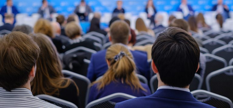 Attendees at a conference seen from the back of the auditorium.
